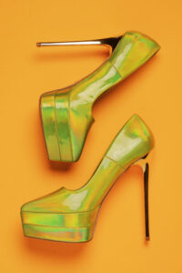 A pair of neon green high heels positioned on a orange background.