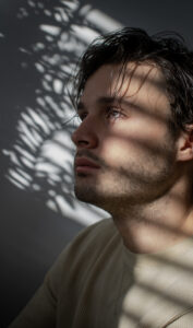 A serious young man gazing upwards while the reflection of the sun shines on his face.